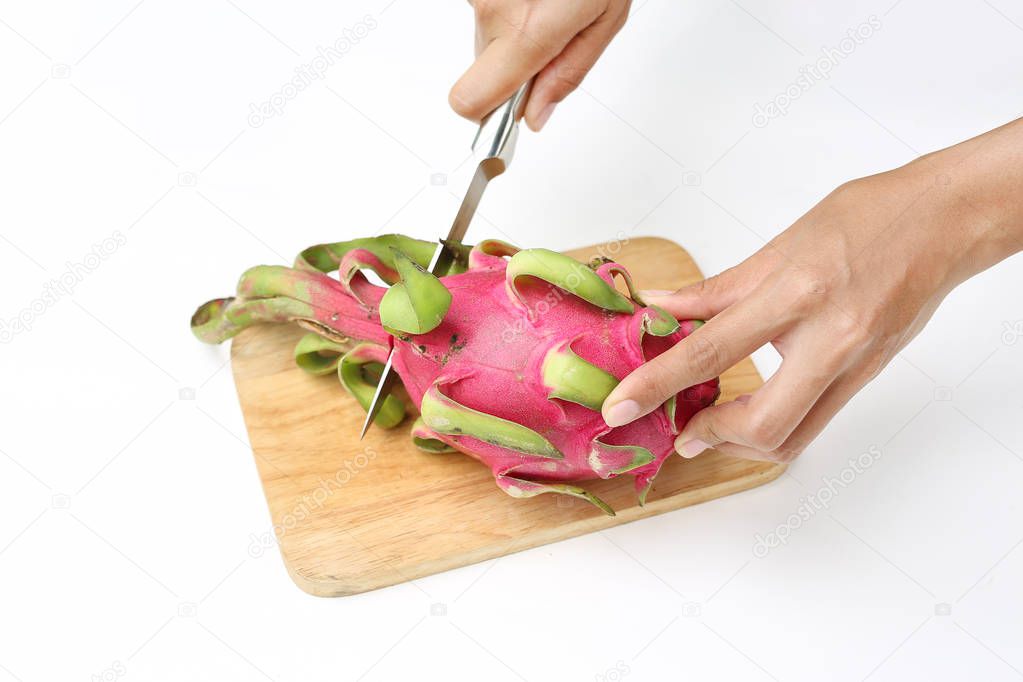 Woman hands cutting dragon fruit on chopping board against white background.