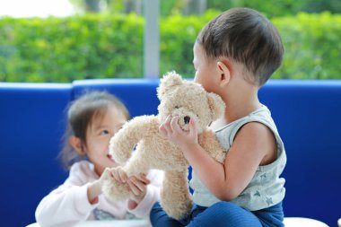 Asian sister scrambling teddy bear with her little brother. clipart