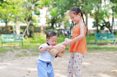 Portrait of little Asian sister scrambling teddy bear with her little brother in the garden outdoor. clipart