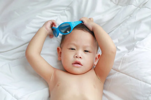 肖像小男孩与太阳镜躺在床上的白色毯子 — 图库照片