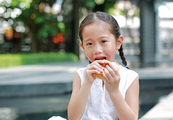 快乐的亚洲小女孩吃面包与填充草莓填充甜点和沾染在她的嘴在花园户外 — 图库照片
