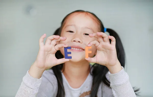 Adorable little Asian child girl holding alphabet EF (Executive Functions) text on her face. Education and development concept.