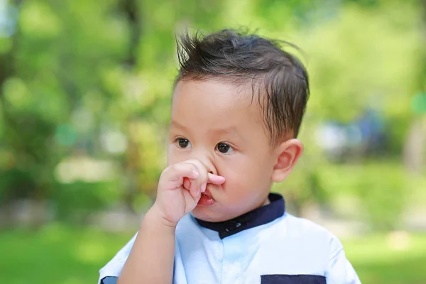 Asyalı küçük çocuk kaşıntılı hissettiği için burnunu parmaklarıyla ovuyor. Burnunu dışarıda kaşıyan yakın çekim çocuk.
