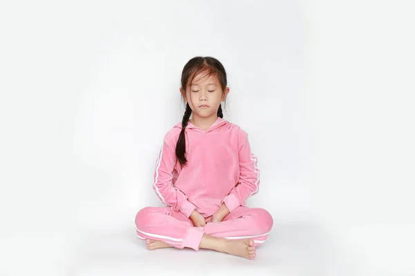 Pembe eşofmanlı ya da spor giysili güzel Asyalı kız çocuğu portresi meditasyonda ve beyaz arka planda barış içinde oturuyor. Huzurlu konsept.