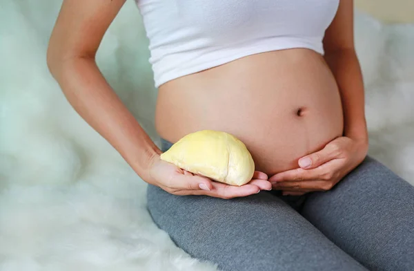 孕妇坐在沙发上 肚子上抱着榴莲 节食的概念 — 图库照片