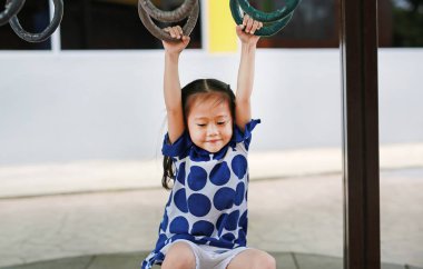 Küçük tatlı Asyalı kız jimnastik yüzüğünde asılı duruyor.