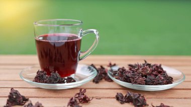 Roselle suyu bardakta ve kuru roselle tahta üzerinde yeşil çimen arka planında.