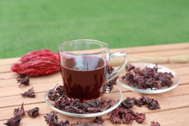 Roselle suyu bardakta ve kuru roselle tahta üzerinde yeşil çimen arka planında.