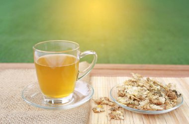 Krizantem suyu cam bardakta ve kurutulmuş kasımpatı çiçeği ahşap arka planda yeşil çimen arka planında