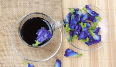 Şeffaf bardakta kelebek bezelye suyu ve çuval üzerinde çiçekler, ahşap kaplama. Üst görünüm