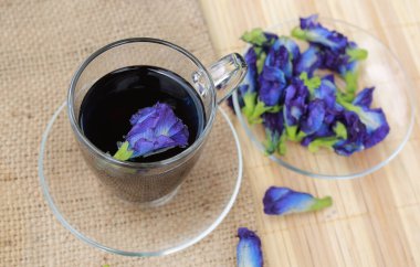 Şeffaf bardakta kelebek bezelye suyu ve tahta zemin üzerinde çiçekler..