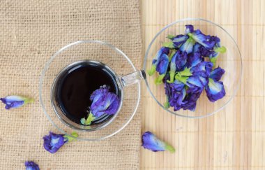 Şeffaf bardakta kelebek bezelye suyu ve çuval üzerinde çiçekler, ahşap kaplama. Üst görünüm