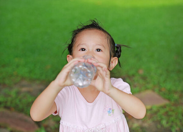 Закройте маленькую девочку, пьющую воду из бутылки в парке. Портрет открытый
.