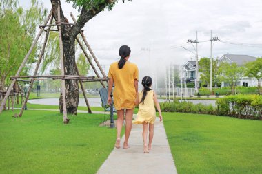 Anne ve kızın arkası el ele, bahçede yürürken rahatlıyor. Anne ve çocuk yaz parkında birlikte vakit geçiriyorlar.