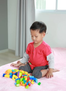 Sevimli Asyalı küçük erkek bebek renkli plastik bloklar oynuyor ve oturduğu yere W-bakıcılığı deniyor. Kötü bir pozisyonda oturan çocuk kalça çıkıklığına neden olabilir..