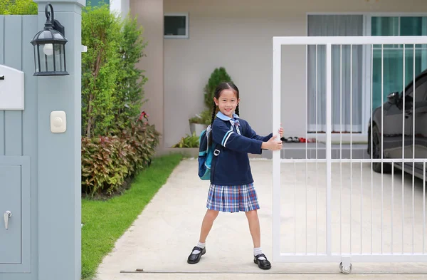 身着幼稚园制服的快乐的亚洲小女孩 在早晨离家上学之前 试图用推拉和拉开房屋的门栅栏来关闭或打开 — 图库照片