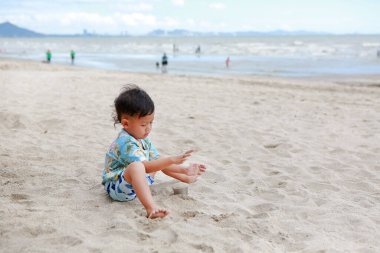 Küçük Asyalı çocuğun plajda kumla eğlenen portresi..