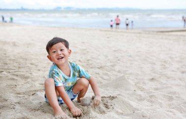 Gülümseyen küçük Asyalı bebek kumsalda kum kazarken iyi eğlenceler..