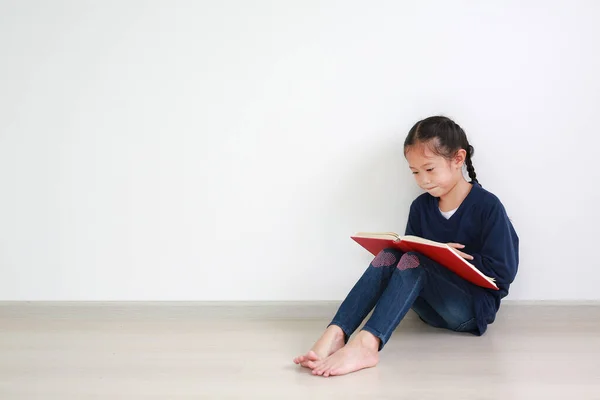 ポートレートアジアの小さな子供の女の子で学校制服読書A本と座っています反対側に白い壁でザ部屋にコピースペース — ストック写真