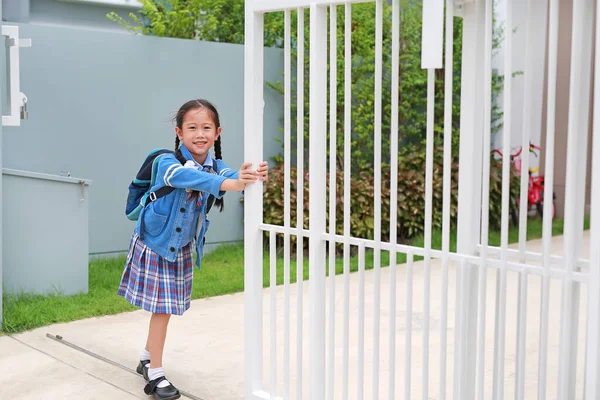 穿着校服的快乐的亚洲小女孩的画像 试图用推拉和拉开房屋的门栅栏 然后在早上离家去学校之前关上或打开 — 图库照片