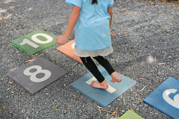 Close-up feet of little girl play jumping on colourful hopscotch playground markings numbers on stone at pavement.