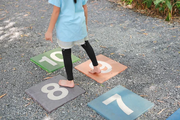 Close-up feet of little girl play jumping on colourful hopscotch playground markings numbers on stone at pavement.