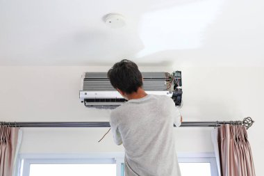 Teknisyen odadaki beyaz duvara yeni klima takmaya hazırlanıyor..