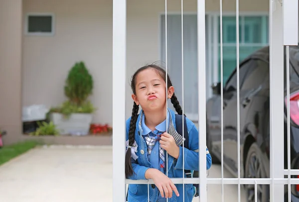 早上上学前 穿着幼稚园制服的亚洲小女孩在家门口的篱笆边 脸上挂着滑稽的表情 — 图库照片