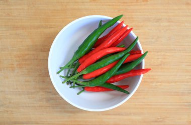 Kırmızı ve yeşil biberler beyaz kasede bambu ahşap arka planda, kırmızı ve yeşil biber pişirmek için kırmızı biber hazırlama süreci. Üst görünüm.