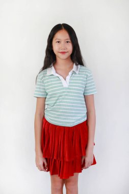 Gülümseyen Asyalı kız, beyaz stüdyo geçmişine karşı duran, en sevdiği kıyafetiyle kendini neşeli ve neşeli hissediyor..