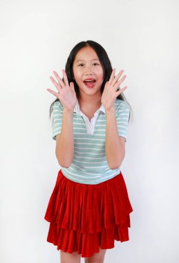 Asyalı kız beyaz arka planda şaşkınlık veya heyecan ifadesi sergiliyor. Çocuk ellerini kaldırırken neşeli ve neşeli bir yüz ifadesi takınıyor..