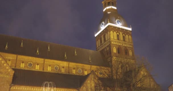 Riga, Letonia - 18 de diciembre de 2017: Gente caminando cerca del tradicional mercado de Navidad en la Plaza de la Cúpula con la Catedral de la Cúpula. Monumento famoso en la noche de invierno en iluminaciones festivas Iluminación — Vídeo de stock