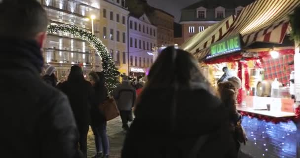 Riga, Lettland - 18. Dezember 2017: Menschen spazieren auf dem traditionellen Weihnachtsmarkt auf dem Domplatz. Handelshäuser in der Winternacht — Stockvideo