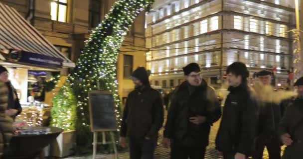 Riga, Lettland - 18. Dezember 2017: Menschen spazieren auf dem traditionellen Weihnachtsmarkt auf dem Domplatz. Handelshäuser in der Winternacht — Stockvideo