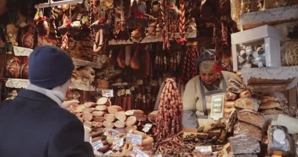 Tallinn, Estland - 22. Dezember 2017: Verkäuferin auf traditionellem Weihnachtsmarkt verkauft Wurst und andere Fleischprodukte auf dem Rathausplatz. Verkäufer bedient Käufer auf lokalem Lebensmittelmarkt — Stockvideo