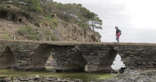 Cadaques, Girona tartomány, Katalónia, Spanyolország. Fiatal nő Tourist Walking On Stone Bridge to Mirador. — Stock videók