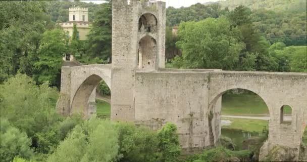 Besalu, Girona, Cataluña, España. Famoso monumento antiguo medieval románico Besalu puente sobre el río Fluvia en el día nublado de verano — Vídeo de stock