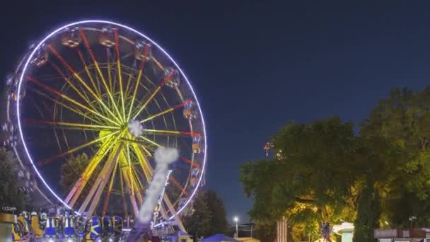 街の遊園地で夏の夜にイルミネーションアトラクション観覧車と明るいカルーセルメリーゴーランドを回る — ストック動画