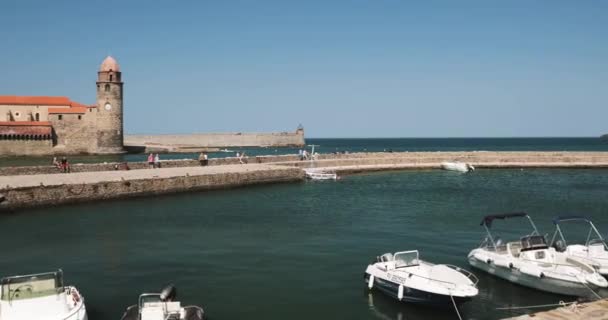 Collioure, France - Le 16 mai 2018 : Des touristes se reposent et marchent sur la côte près de l'église Notre-Dame des Anges à travers la baie au printemps — Video