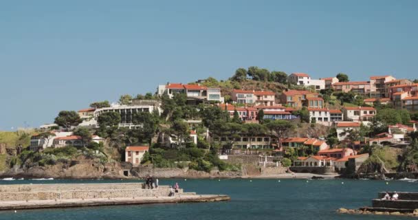 Collioure, Frankreich. Blick vom Liegeplatz in Port nach Collioure Hügeliges Stadtbild im sonnigen Frühling. Touristen, die sich ausruhen und an der Küste über die Bucht laufen — Stockvideo