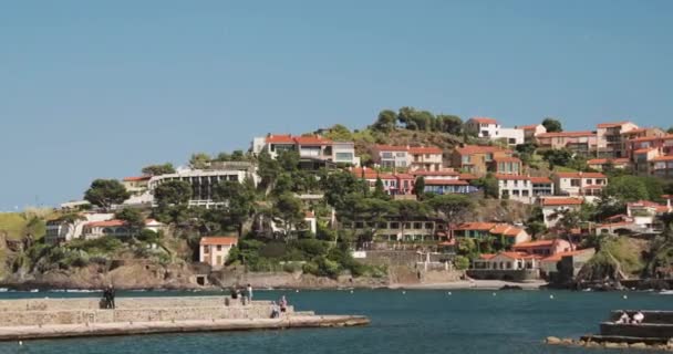 Collioure, Francie. Pohled z kotviště v přístavu do Collioure Hilly Cityscape ve slunečném jaru Evropy. Lidé Turisté odpočinku a procházky v pobřeží přes záliv — Stock video