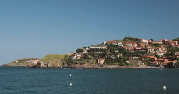 Collioure, Francie. Pohled z kotviště v přístavu do Collioure Hilly Cityscape ve slunečném jaru Evropy. Lidé Turisté odpočinku a procházky v pobřeží přes záliv — Stock video