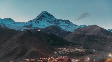 Stepantsminda, Georgia. Karla kaplı Kazbek Dağı tepesi, ünlü Gergeti Kilisesi ve Gece Yıldırımları Kırsal Evler. Gürcistan Manzarası