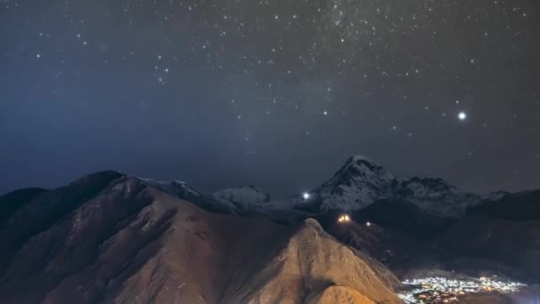 Stepantsminda, Georgia. Cielo estrellado nocturno con estrellas brillantes sobre el pico del monte Kazbek cubierto de nieve. Famosa iglesia Gergeti en relámpago nocturno. Hermoso paisaje georgiano — Vídeos de Stock