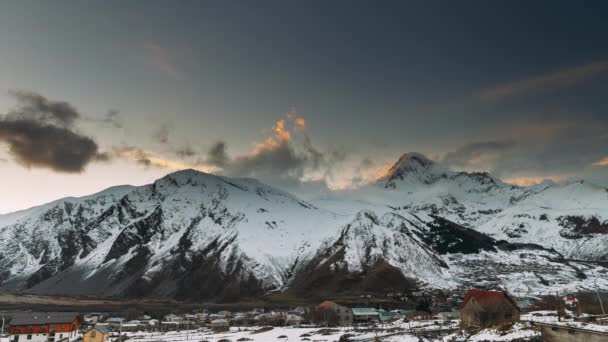 Stepantsminda, Georgien. Gipfel des Kasbek bei Sonnenuntergang. Berühmte Gergeti-Kirche und Landhäuser an Winterabenden. Georgische Landschaft — Stockvideo