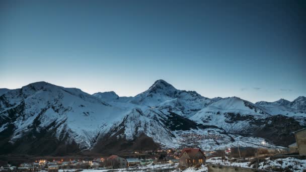 Stepantsminda, Georgia. Notte invernale cielo stellato con stelle incandescenti e picco del Monte Kazbek coperto di neve. Bella notte georgiano paesaggio invernale — Video Stock