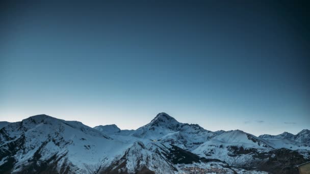 Stepantsminda, Georgia. Zimní noční hvězdné nebe se zářícími hvězdami a vrcholem hory Kazbek pokryté sněhem. Krásná noc gruzínská zimní krajina — Stock video