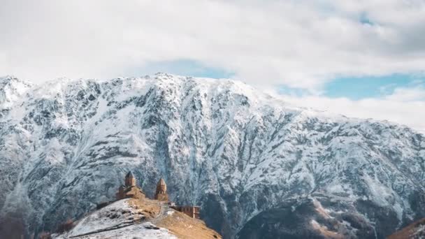 Stepantsminda, Gergeti, Georgia. Famosa Gergeti Trinity Tsminda Sameba Church In Early Winter Landscape. Hermoso paisaje georgiano a principios de invierno — Vídeos de Stock