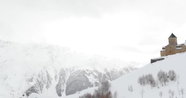 Stepantsminda, Gergeti, Georgia. Hergeti Trinity Tsminda Sameba Church In Winter Landscape — стокове відео