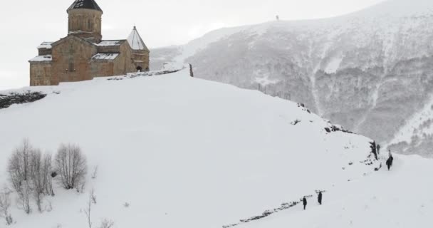 格鲁吉亚Gergeti的Stepantsminda 在冬季景观中走在著名的Gergeti Trinity Tsminda Sameba教堂附近的人 — 图库视频影像